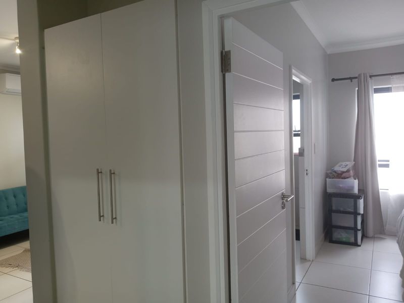 A view of a hallway featuring built-in cupboards and modern interior doors, leading into adjacent living and bedroom spaces with tiled flooring.