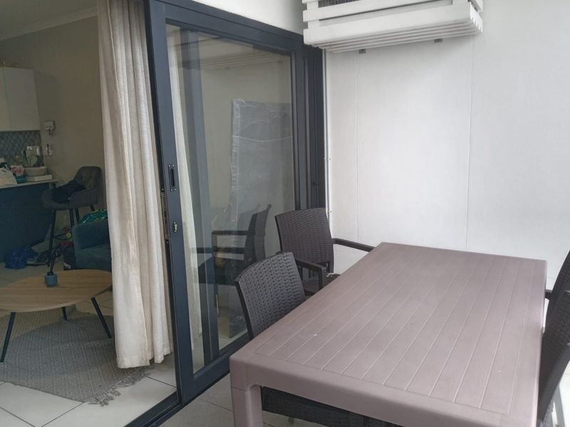 A covered balcony area featuring a sliding glass door entrance, tiled flooring, and a wall-mounted air conditioning unit.