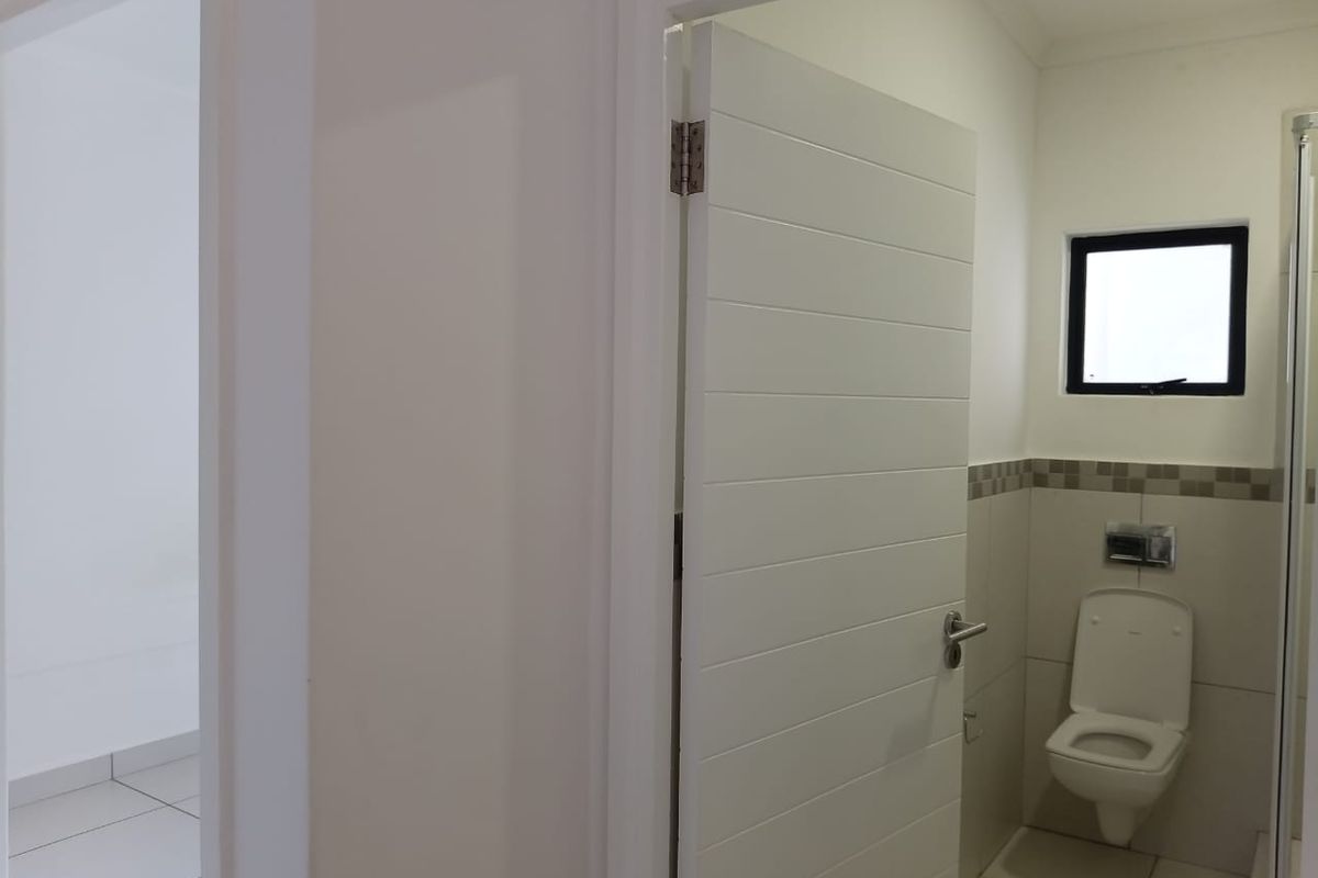 A clean, modern bathroom featuring a wall-mounted toilet, tiled walls with a decorative border, and a window for natural light.