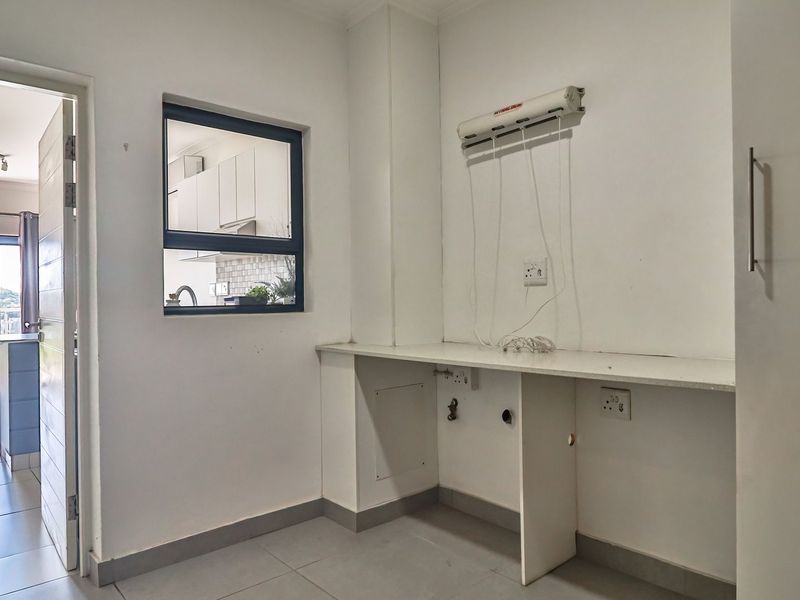 A functional laundry area featuring a built-in countertop, plumbing connections for appliances, and a wall-mounted drying rack, with tiled flooring throughout.
