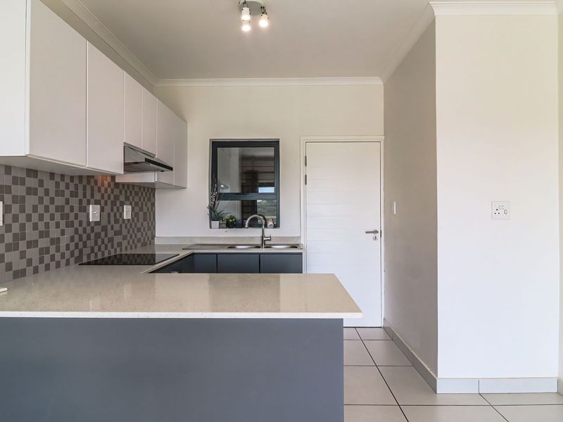 Modern kitchen featuring sleek grey and white cabinetry, stone countertops, a tiled backsplash, and integrated hob with extractor fan.