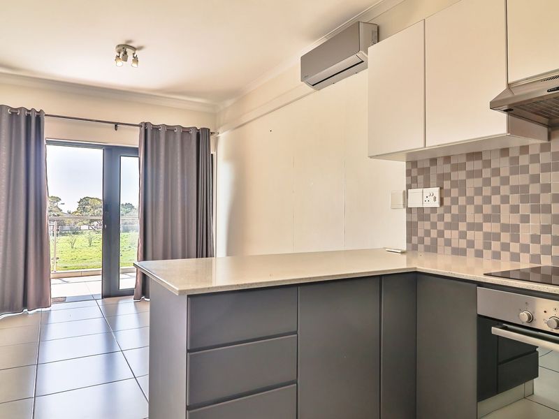 Modern open-plan kitchen and living area featuring sleek cabinetry, stone countertops, integrated appliances, tiled flooring, and direct access to a balcony.