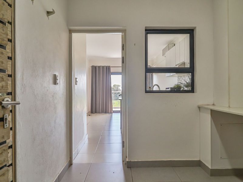 A functional hallway area featuring tiled flooring, an internal window looking into the kitchen, and a built-in counter space.