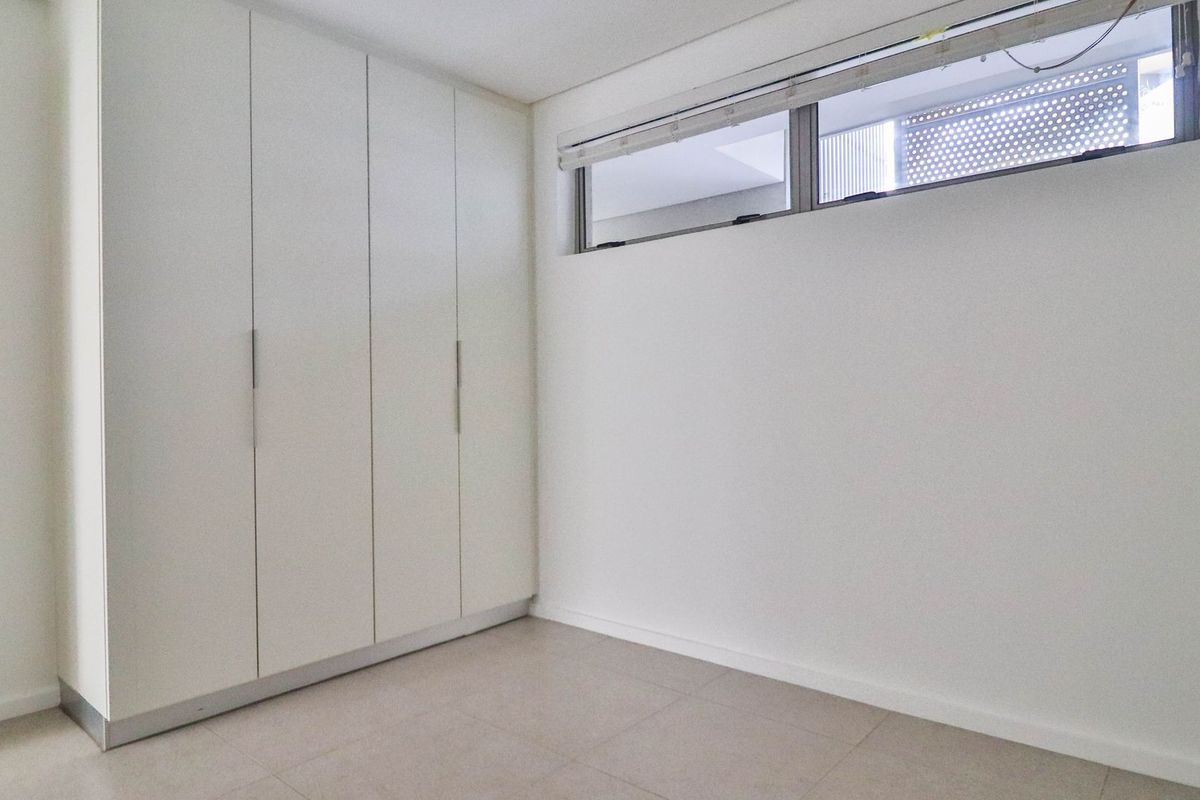 A bright, empty bedroom featuring neutral floor tiles and built-in floor-to-ceiling white cabinetry with modern hardware.