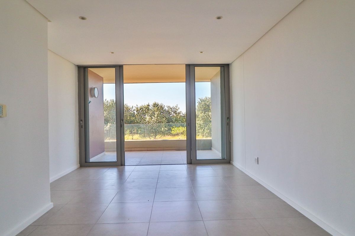 A bright, empty living area featuring large sliding glass doors that open onto a private balcony with scenic outdoor views.