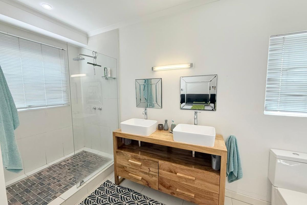 Modern bathroom featuring a double vanity with vessel sinks, a walk-in glass shower with tiled flooring, and dual windows with fitted blinds.