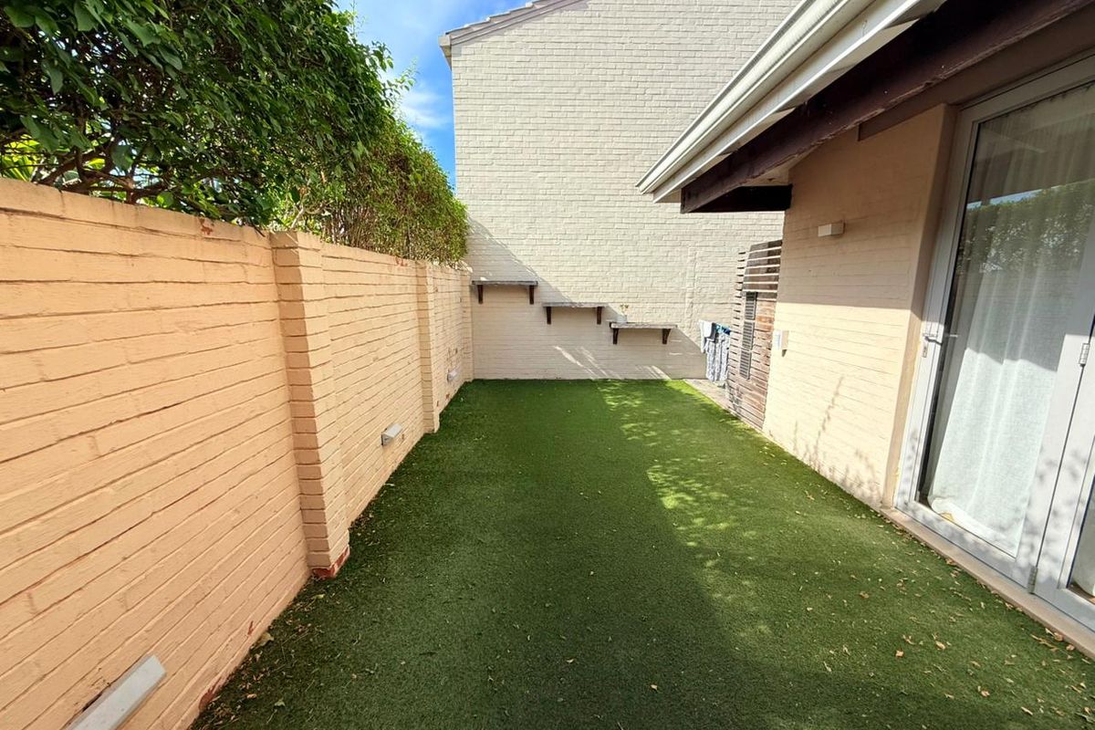 A private rear courtyard featuring artificial turf, a high perimeter brick wall, and direct access to the interior via sliding glass doors.