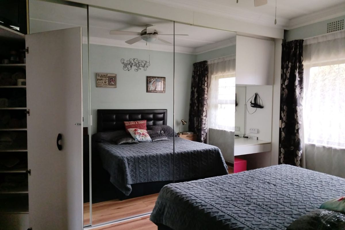 A bedroom featuring extensive floor-to-ceiling mirrored built-in cupboards, a ceiling fan, and a built-in vanity area with integrated lighting.