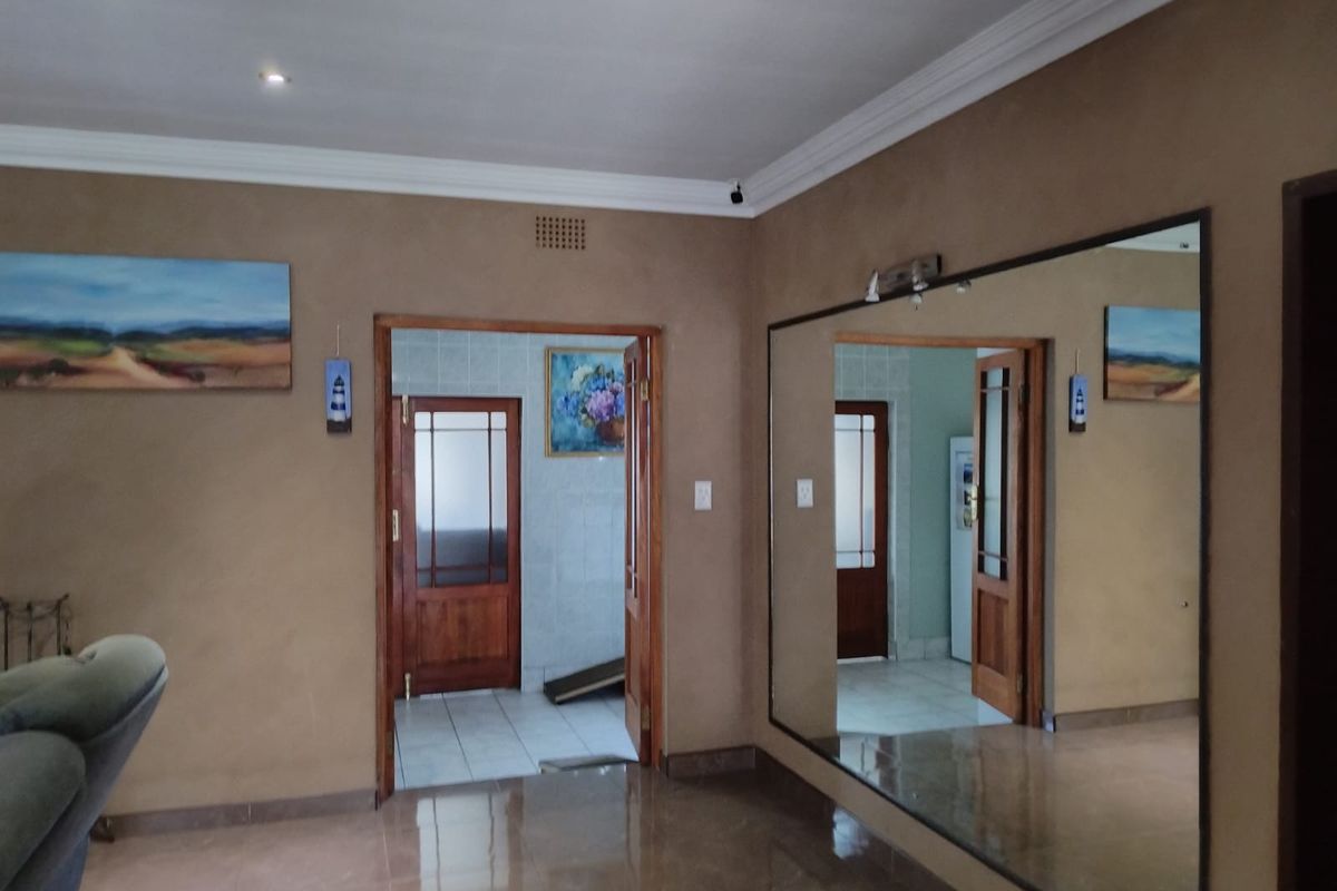 Interior view of a living area featuring tiled flooring, crown molding, and a large wall-mounted mirror leading into an adjacent room with wooden doors.