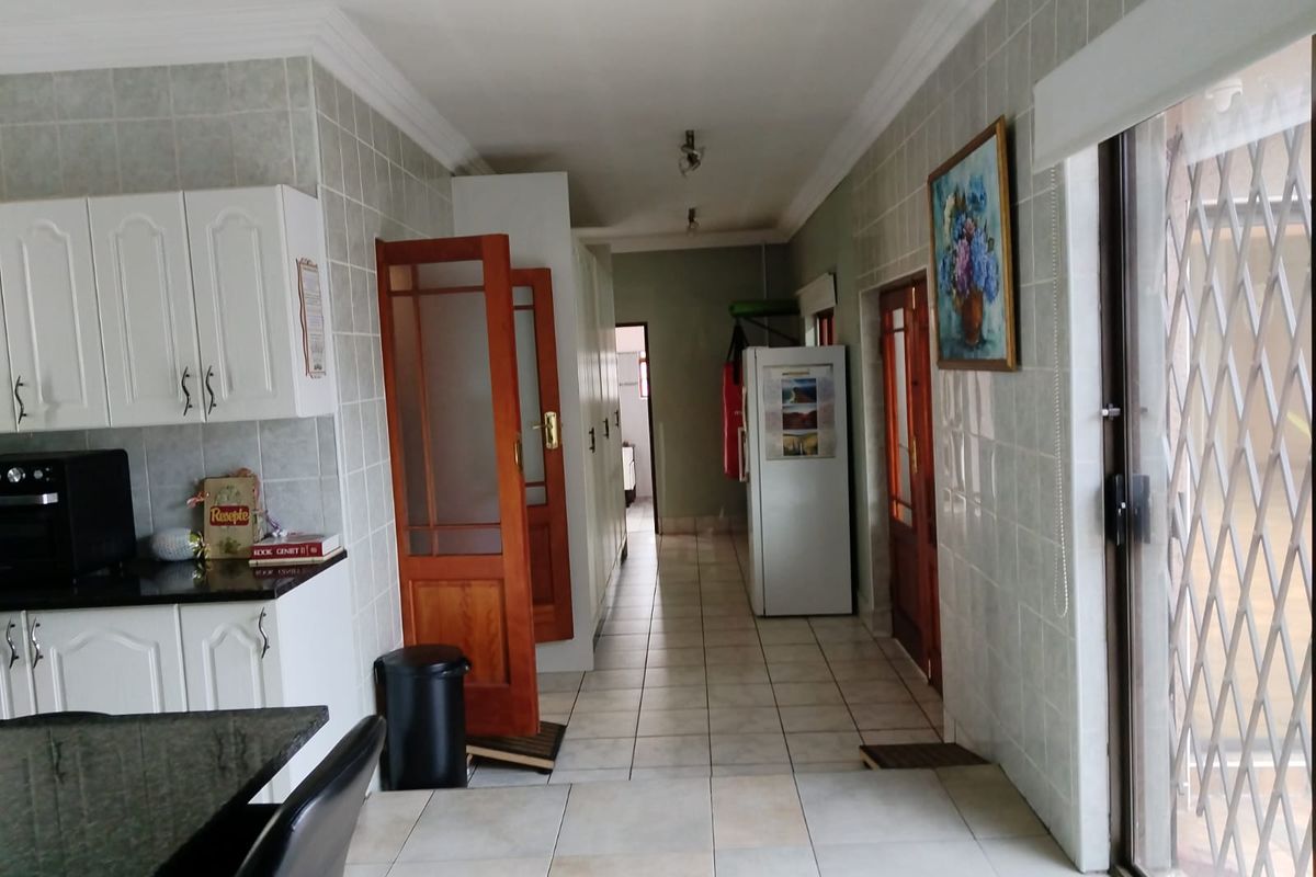 A functional kitchen and hallway area featuring tiled flooring, white cabinetry, and direct access to an outdoor space through a sliding door.