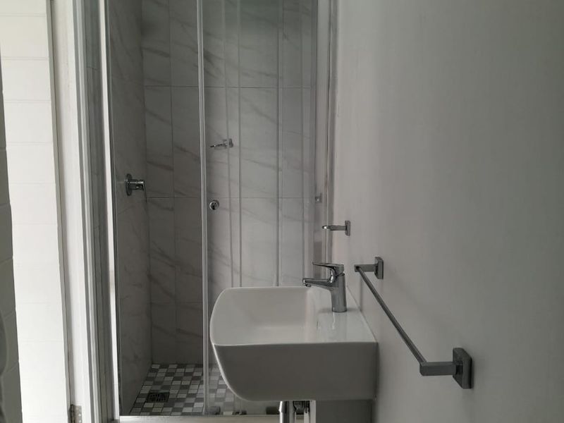 A modern bathroom featuring a pedestal basin, chrome fixtures, and a glass-enclosed shower with marble-look wall tiling.