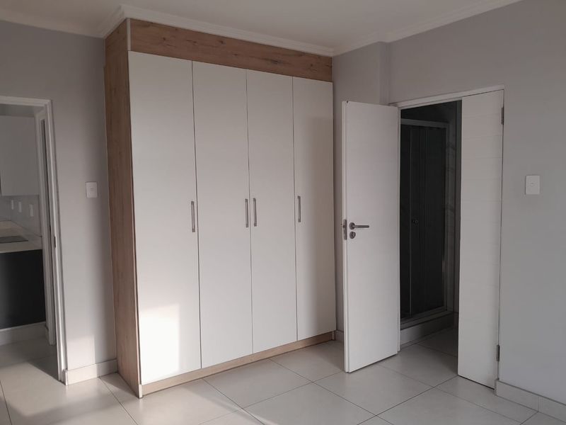 Bedroom featuring modern built-in wardrobes with a wood-grain frame and white doors, tiled flooring, and direct access to an en-suite bathroom.