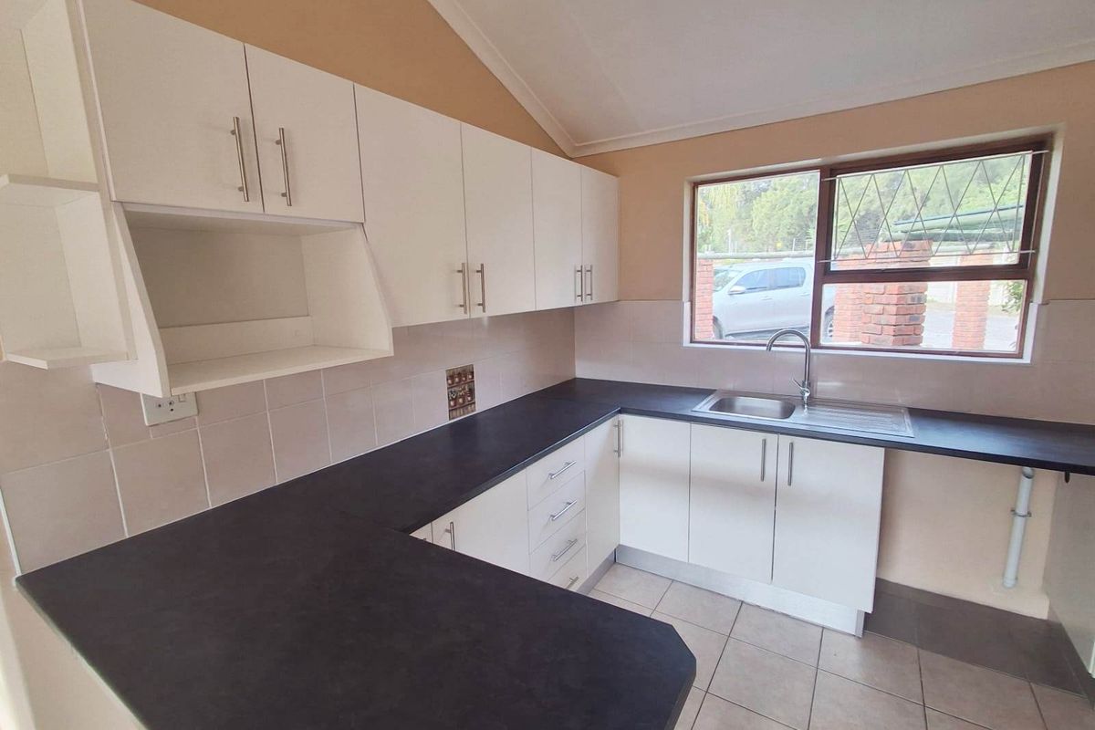 A functional kitchen featuring white cabinetry, dark laminate countertops, tiled splashbacks, and a stainless steel sink with a window view.