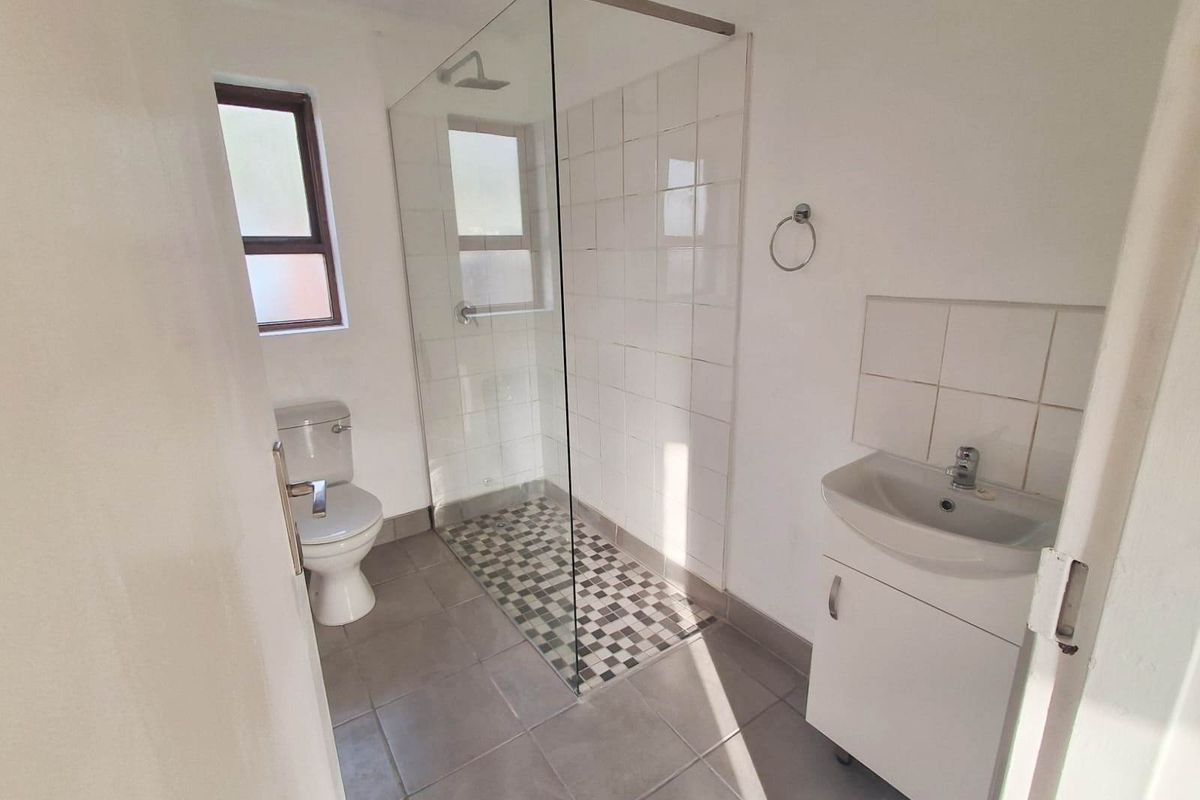 A functional bathroom featuring a walk-in shower with glass enclosure, a pedestal vanity, and a toilet, finished with neutral floor and wall tiling.