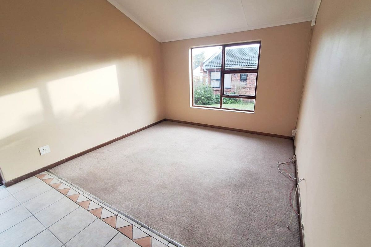 An empty bedroom featuring neutral wall tones, carpeted flooring, and a large window providing natural light and a view of the exterior.