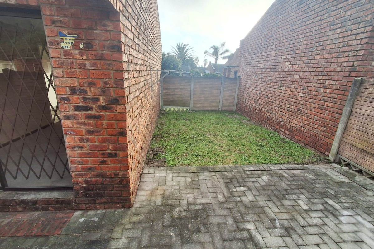 A private rear courtyard featuring a paved patio area, a small lawn, and secure brick boundary walls with a wall-mounted washing line.