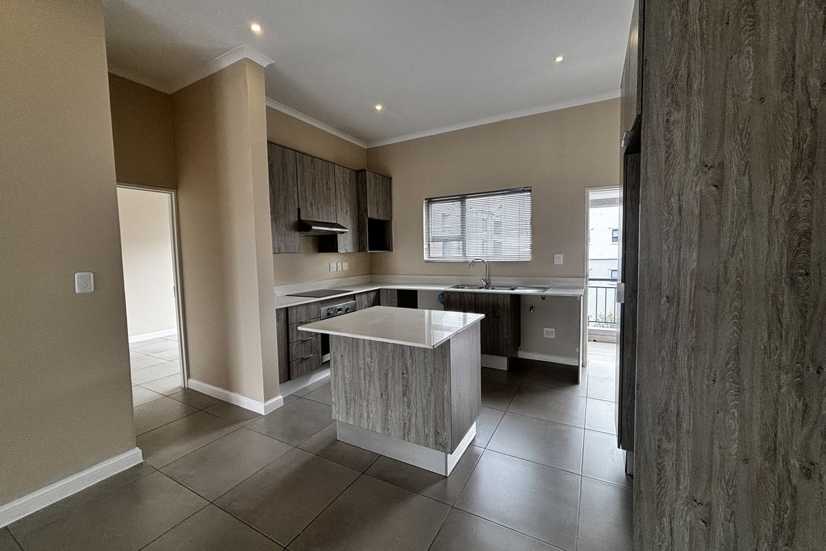 Modern kitchen featuring wood-grain cabinetry, a central island with stone countertop, built-in oven, extractor fan, and tiled flooring.