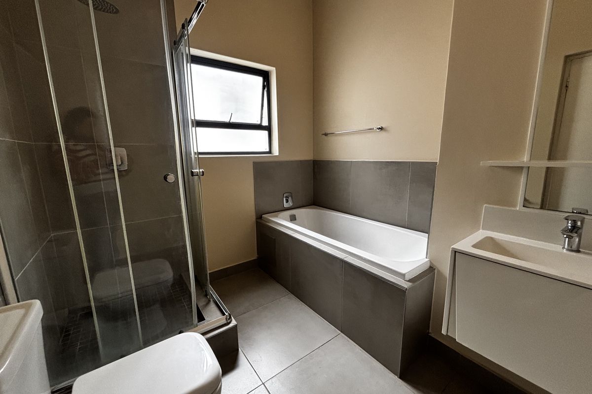 A modern bathroom featuring a glass-enclosed shower, a built-in bathtub with grey tiling, a wall-mounted vanity, and a toilet.