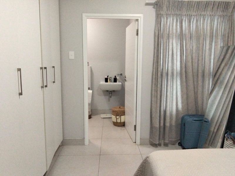 A bedroom featuring built-in wardrobes and an en-suite bathroom with a wall-mounted basin and tiled flooring.