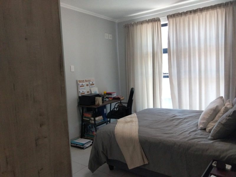 A functional bedroom featuring tiled flooring, neutral wall finishes, and large windows with curtains, providing natural light and a comfortable living space.