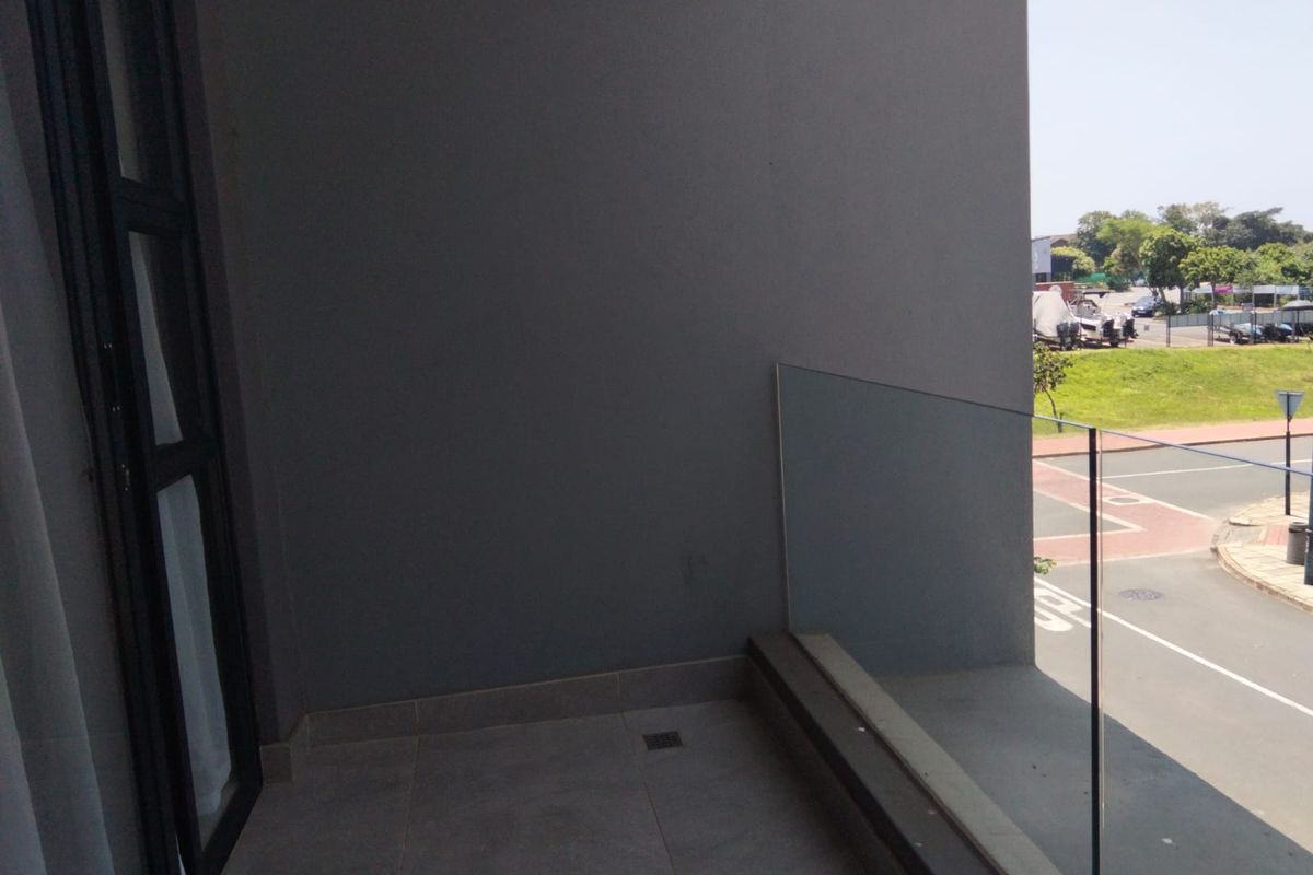 A modern balcony featuring tiled flooring and a frameless glass balustrade, offering an open view of the surrounding street and neighborhood.