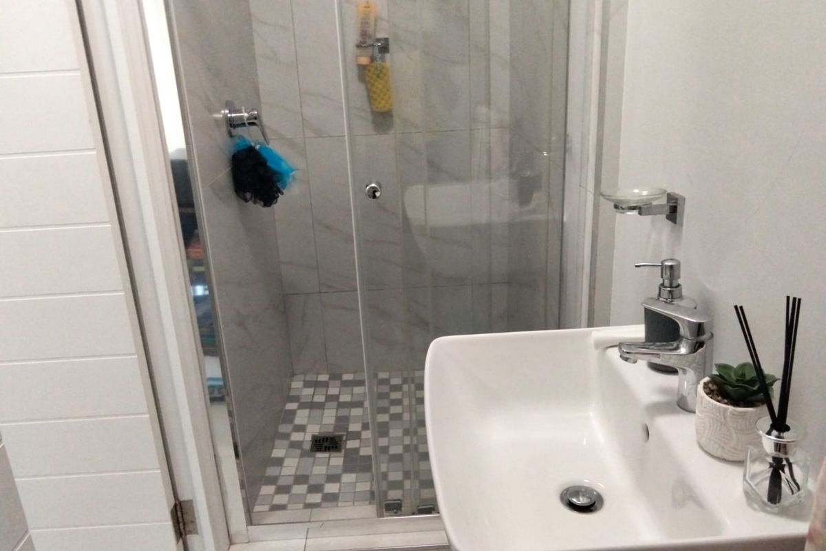 A modern bathroom featuring a glass-enclosed shower with mosaic floor tiling and a contemporary wall-mounted basin with chrome fixtures.