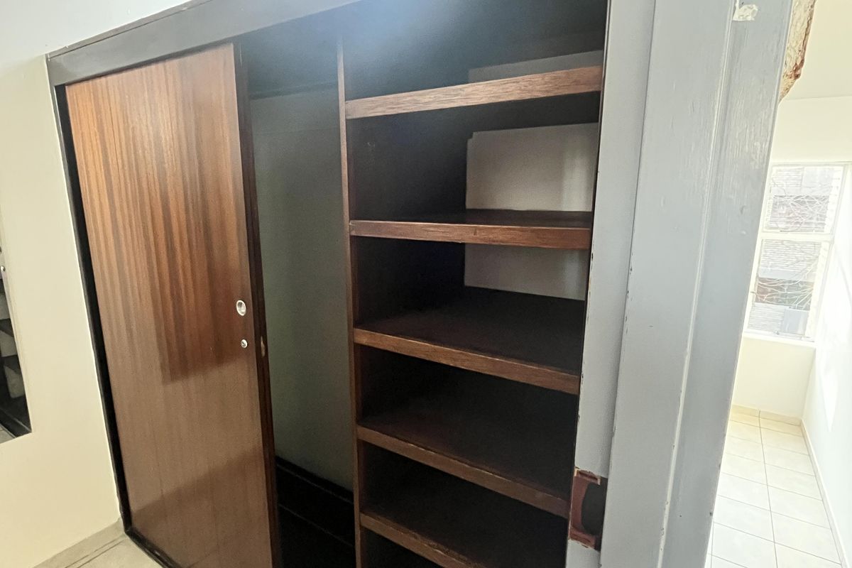 A bedroom featuring a built-in wooden wardrobe with sliding doors and integrated shelving, set against tiled flooring.