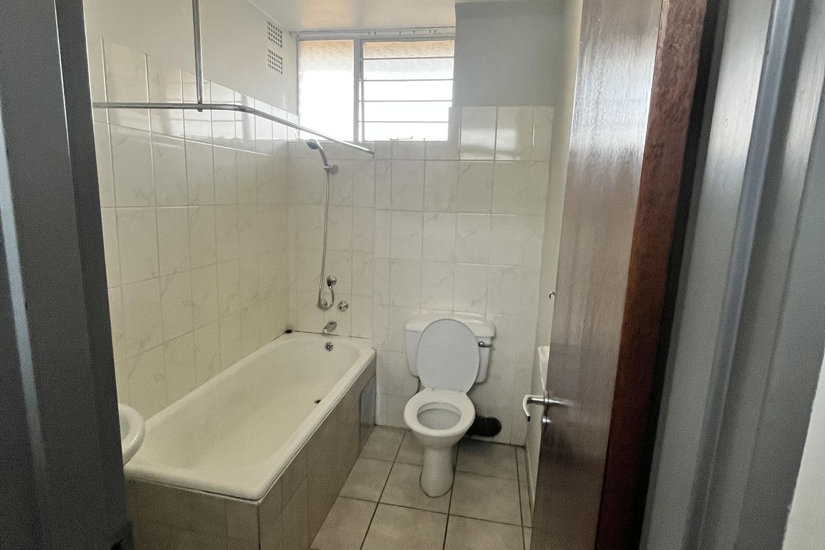 A functional bathroom featuring a bathtub with shower attachment, toilet, and tiled flooring and walls.