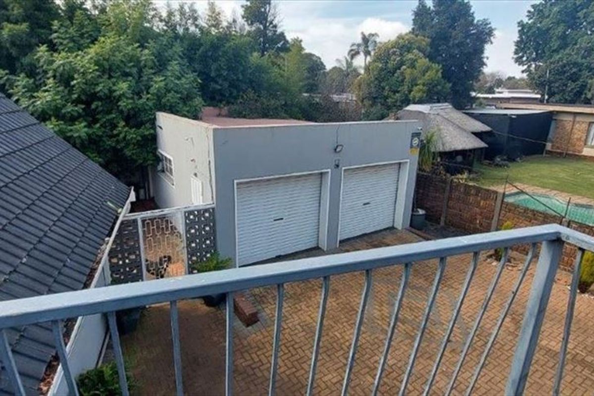 Elevated view overlooking a paved driveway, double garage, and rear garden area featuring a swimming pool and established trees.