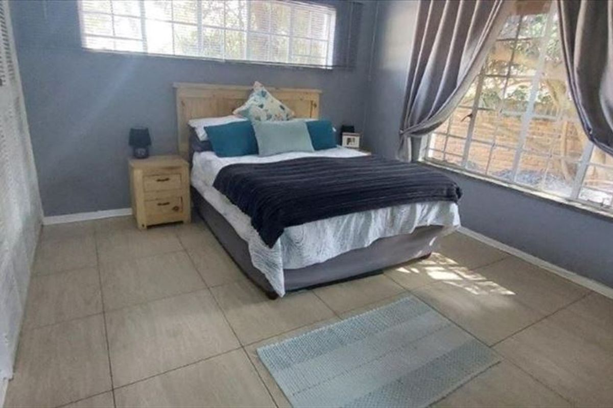 A bedroom featuring tiled flooring, built-in louvered door closets, and large windows allowing natural light.
