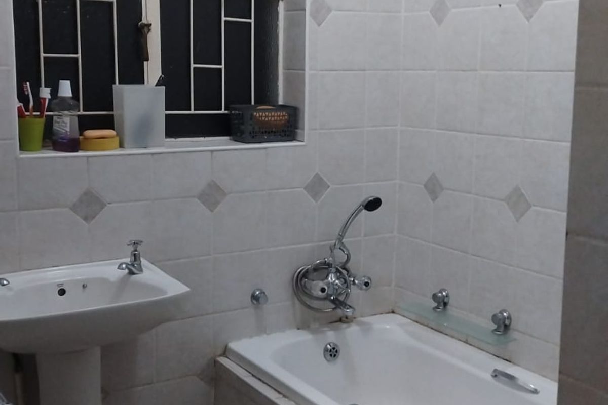 A functional bathroom featuring a pedestal basin, a built-in bathtub with shower mixer, and tiled walls with decorative accents.