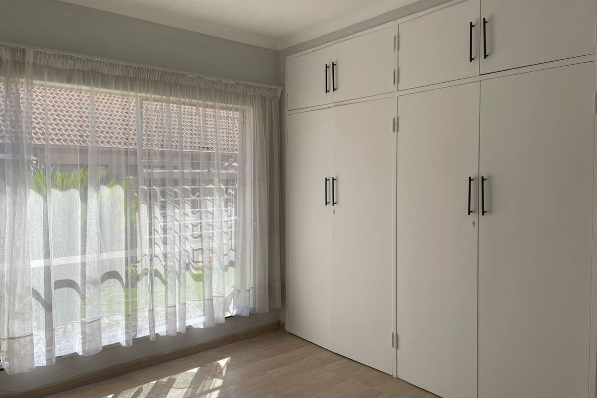 A bright bedroom featuring built-in floor-to-ceiling cabinetry with modern hardware and light-toned laminate flooring.