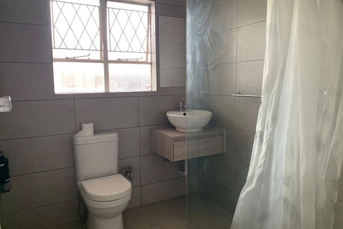 A functional bathroom featuring a wall-mounted vanity with a vessel sink, a toilet, and a shower area with a glass screen.