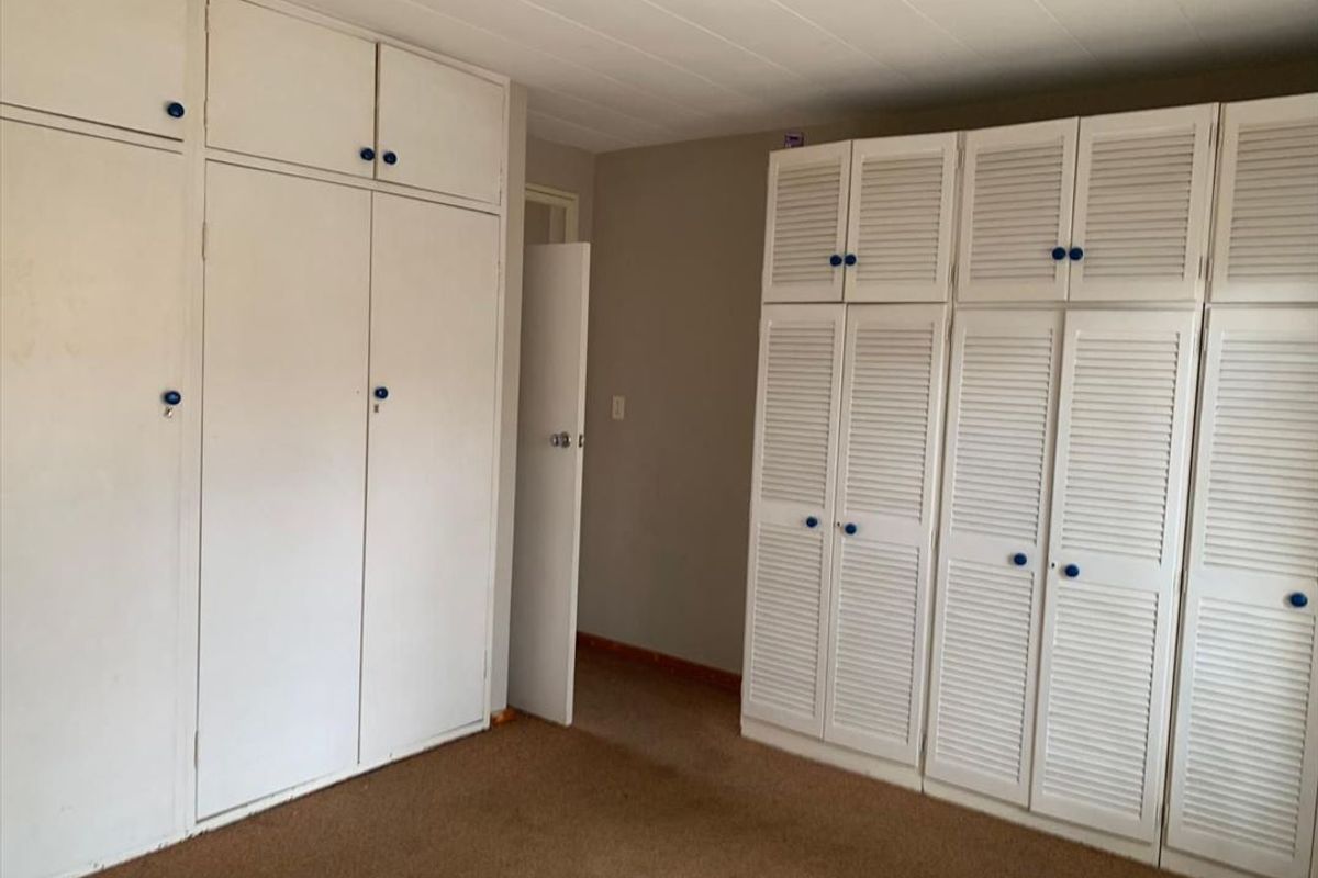 A bedroom featuring extensive built-in storage with white cabinetry and carpeted flooring.