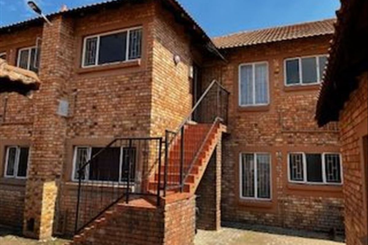 Exterior view of a multi-story townhouse complex featuring face-brick facade, tiled roofing, and an external staircase leading to upper-level access.