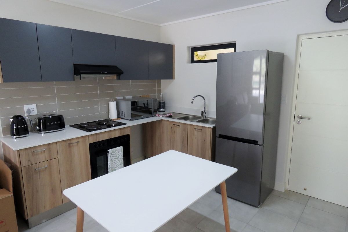 Modern kitchen featuring wood-finish lower cabinets, dark grey upper cabinetry, tiled backsplash, electric hob, built-in oven, and stainless steel sink.