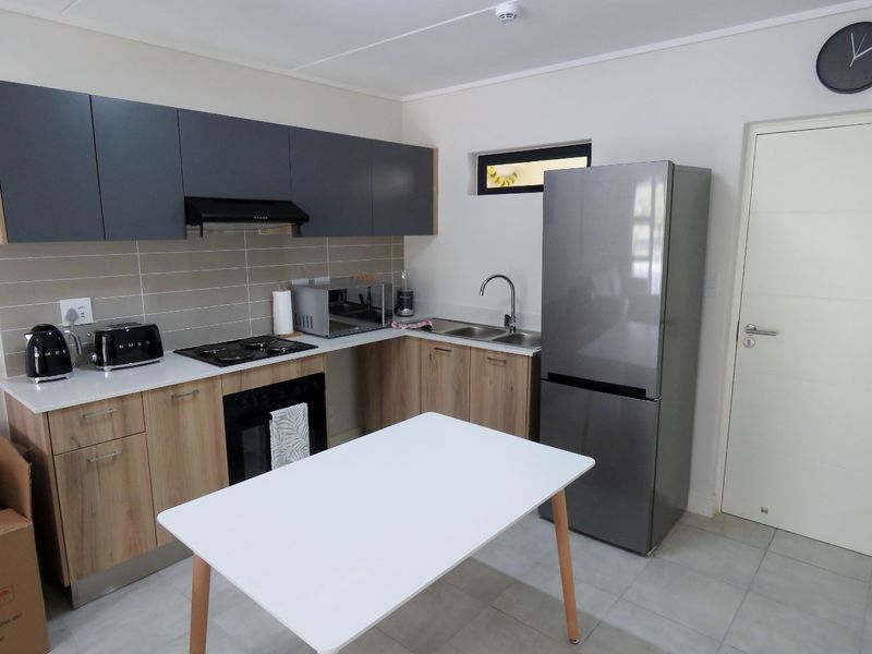 Modern kitchen featuring wood-finish lower cabinets, dark grey upper cabinetry, tiled backsplash, electric hob, built-in oven, and stainless steel sink.