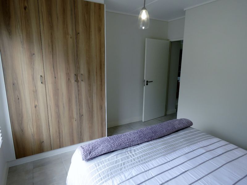 A clean, modern bedroom featuring neutral tiled flooring, a large wood-finish built-in wardrobe, and a contemporary pendant light fixture.