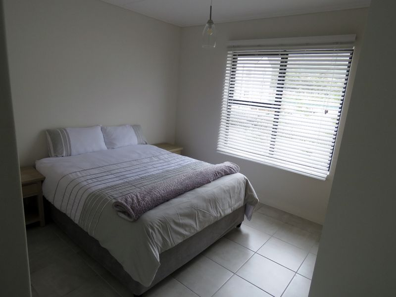 A well-lit bedroom featuring neutral tiled flooring, a large window with venetian blinds, and a modern pendant light fixture.