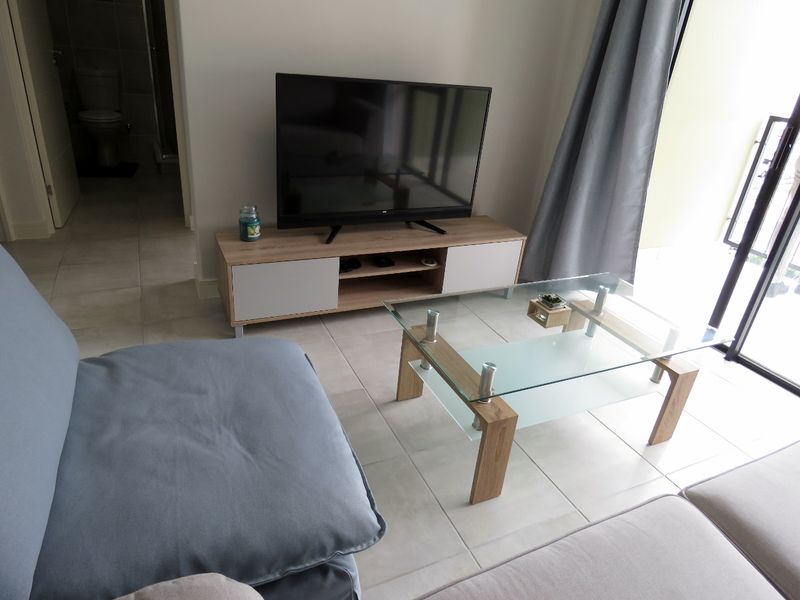 A bright living room area featuring neutral tiled flooring and a sliding glass door providing access to the balcony.