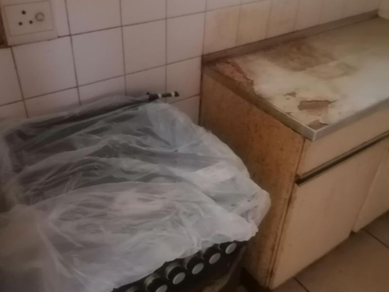 A dated kitchen area featuring tiled splashbacks, laminate countertops, and built-in cabinetry, currently showing significant signs of wear and surface damage.