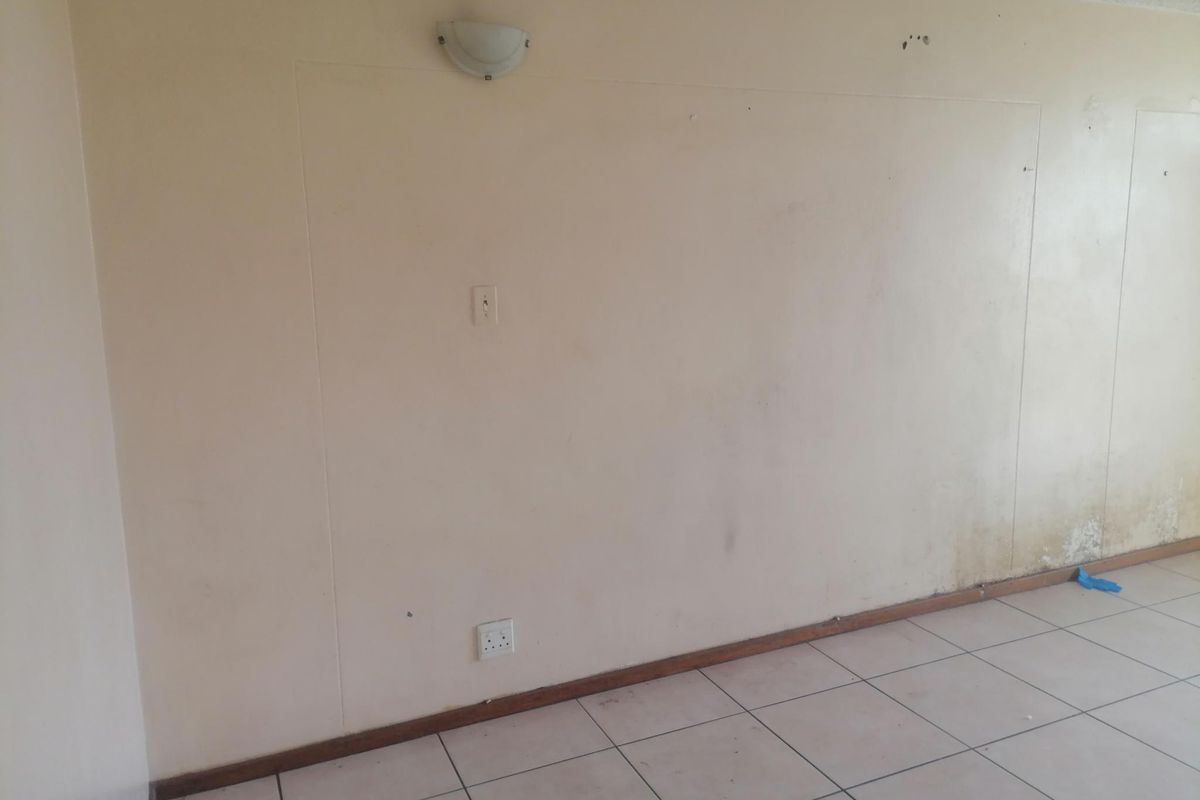 An empty living area featuring tiled flooring and wall-mounted lighting, currently showing signs of wear and surface staining on the walls.