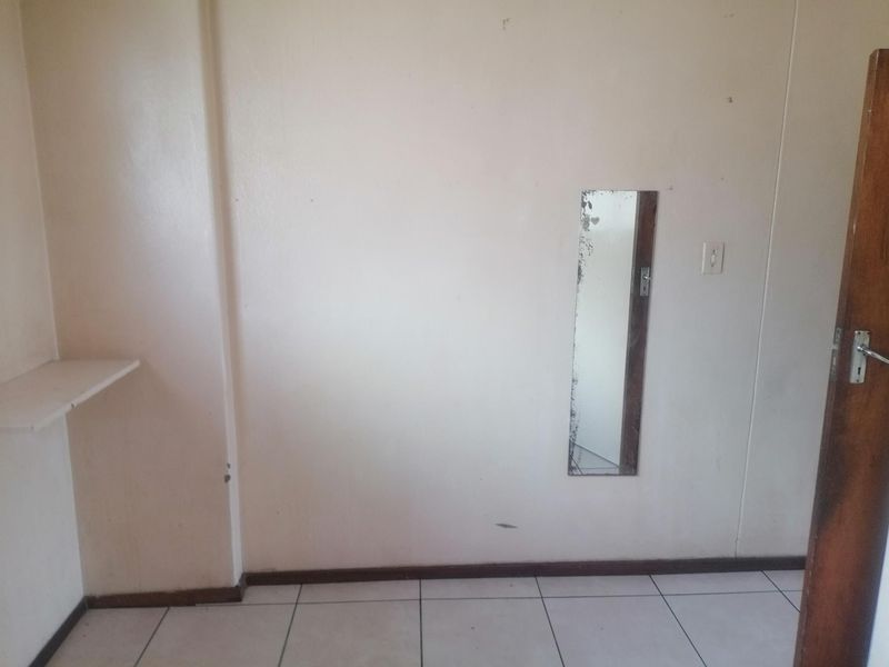 An empty bedroom featuring tiled flooring, a built-in wall shelf, and a wall-mounted mirror, requiring cosmetic updates to improve its overall condition.