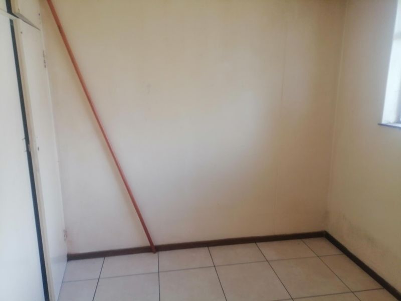 An empty bedroom featuring tiled flooring and a built-in cupboard, requiring cosmetic updates to the walls.