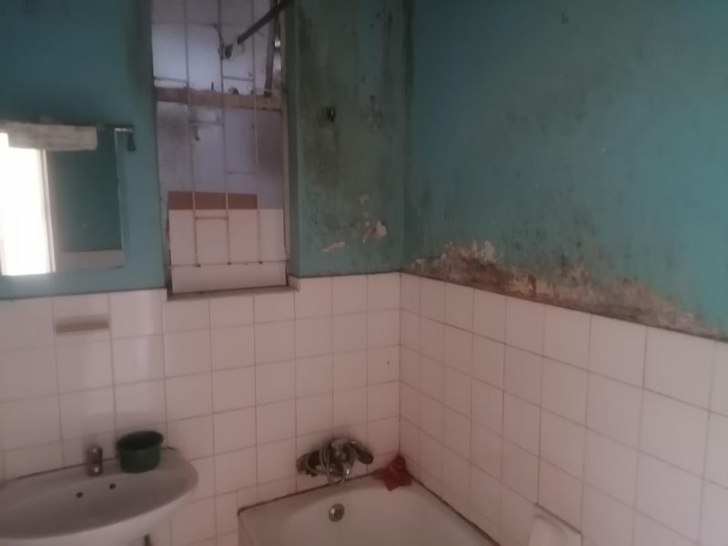 A bathroom featuring a pedestal basin and bathtub, currently showing significant signs of wall dampness and deterioration requiring urgent maintenance and renovation.