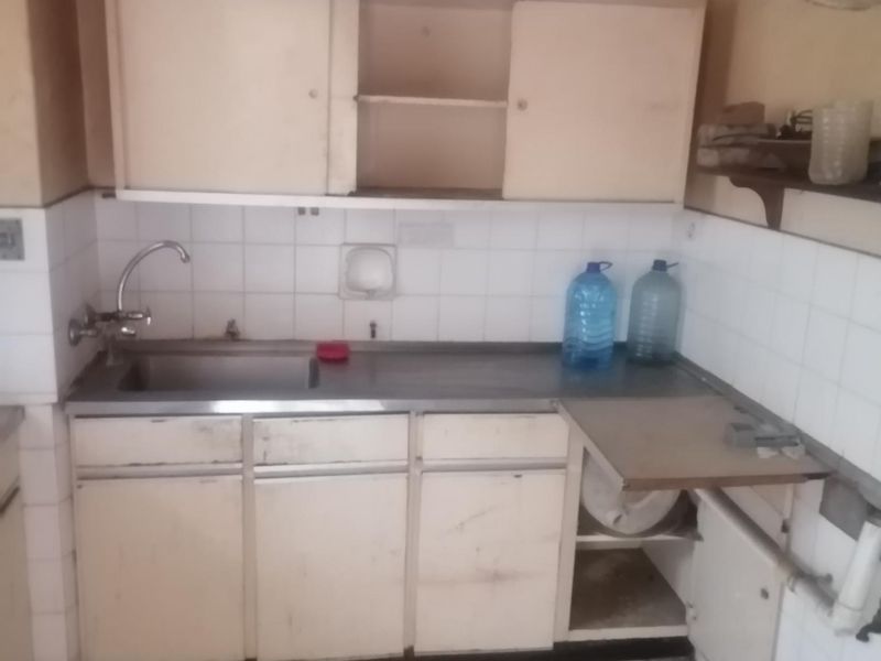 A dated kitchen area featuring basic built-in cabinetry, a stainless steel sink, and tiled finishes, requiring renovation to modernize the space.