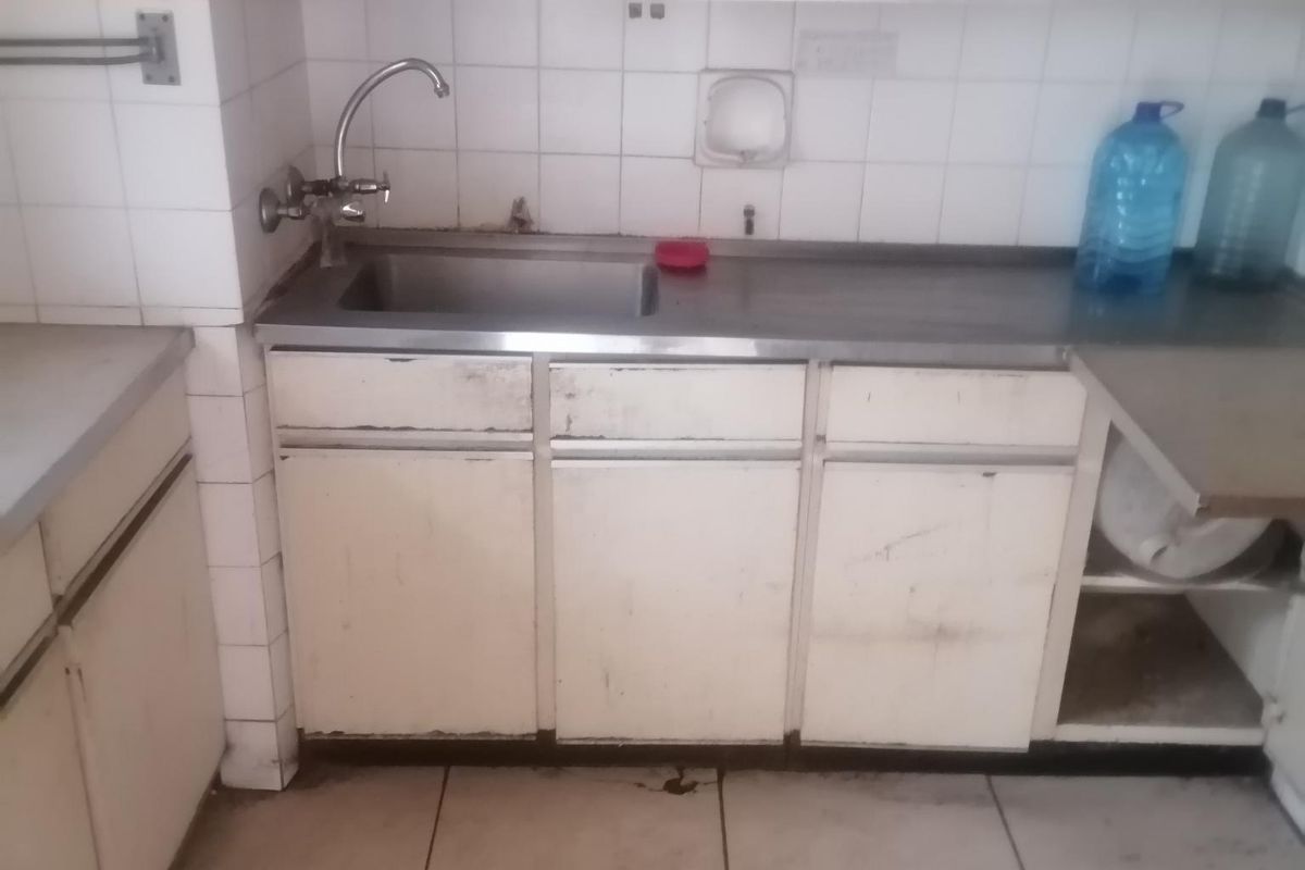 A dated kitchen area featuring built-in cabinetry, a stainless steel sink, and tiled backsplash, requiring significant refurbishment and modernization.