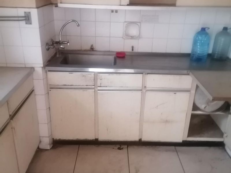 A dated kitchen area featuring built-in cabinetry, a stainless steel sink, and tiled backsplash, requiring significant refurbishment and modernization.