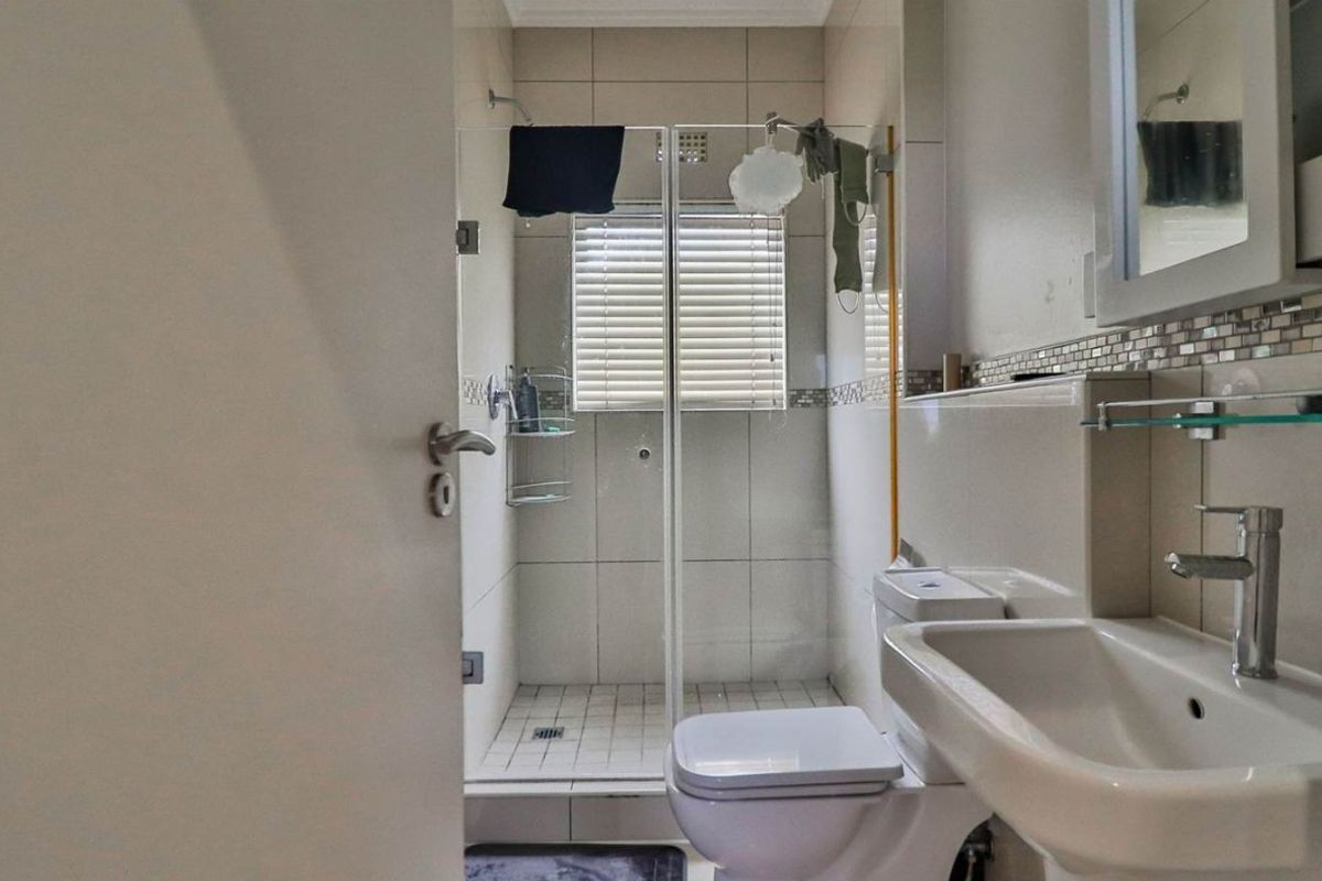 A functional bathroom featuring a glass-enclosed shower, wall-mounted basin, and toilet with neutral wall tiling and a mosaic accent border.