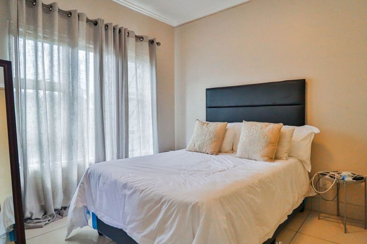A well-lit bedroom featuring tiled flooring, built-in cupboards, and large windows with sheer curtains, providing a comfortable and functional living space.